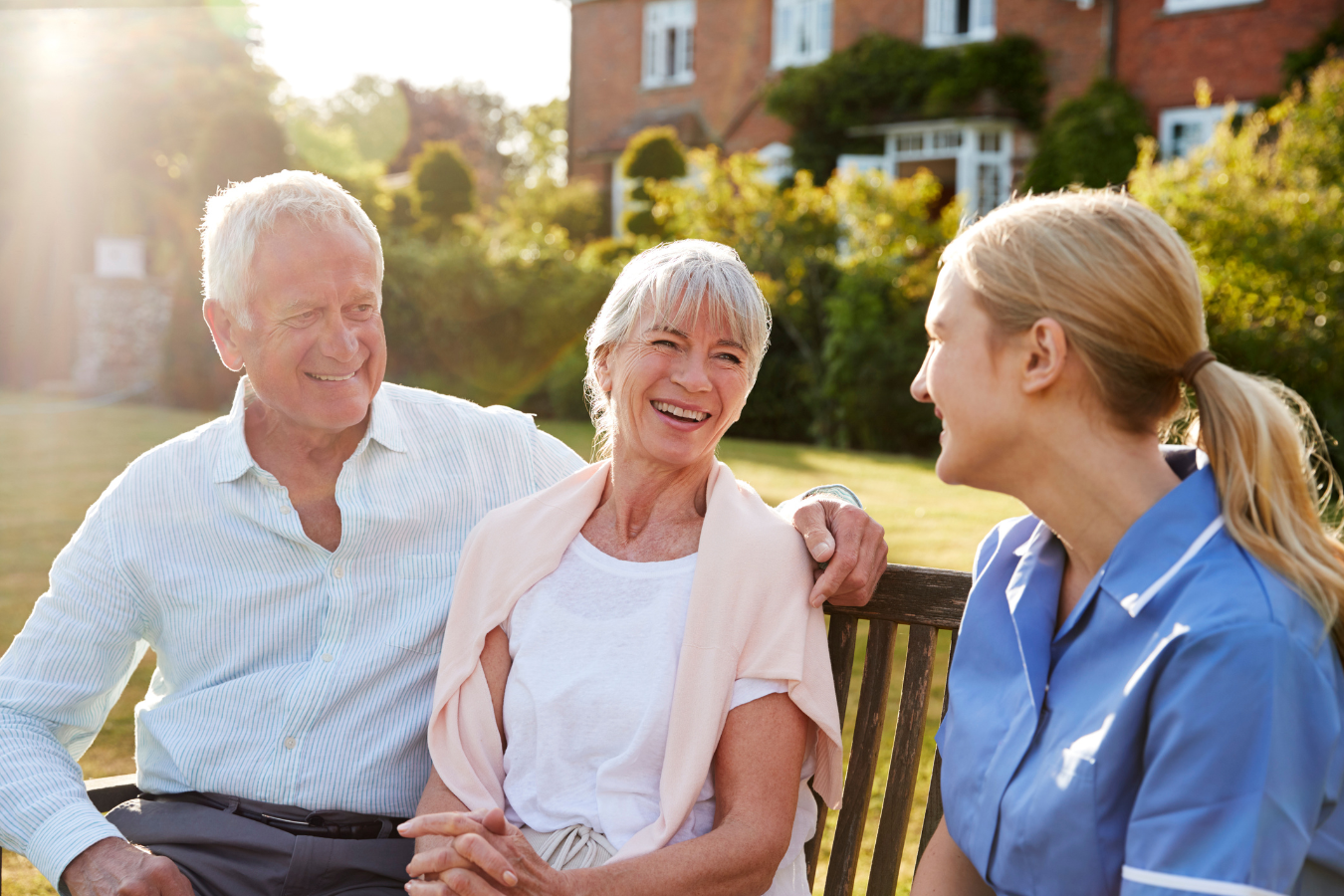 A health care professional assists an adult couple, man and woman, outside at a residential care facility.