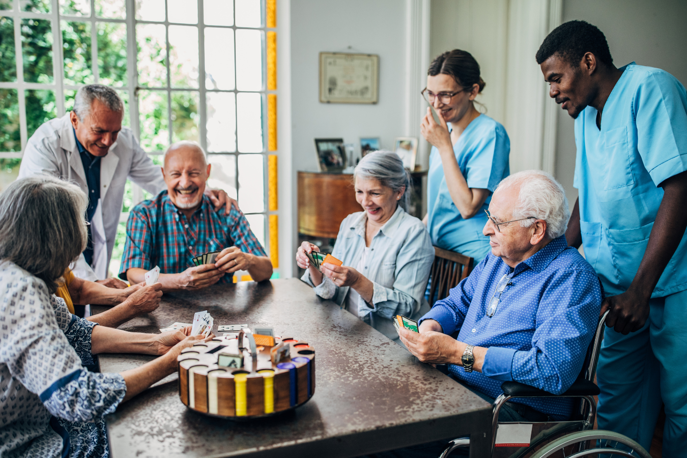 Residents play cards with two health care professionals in a residential care facility.